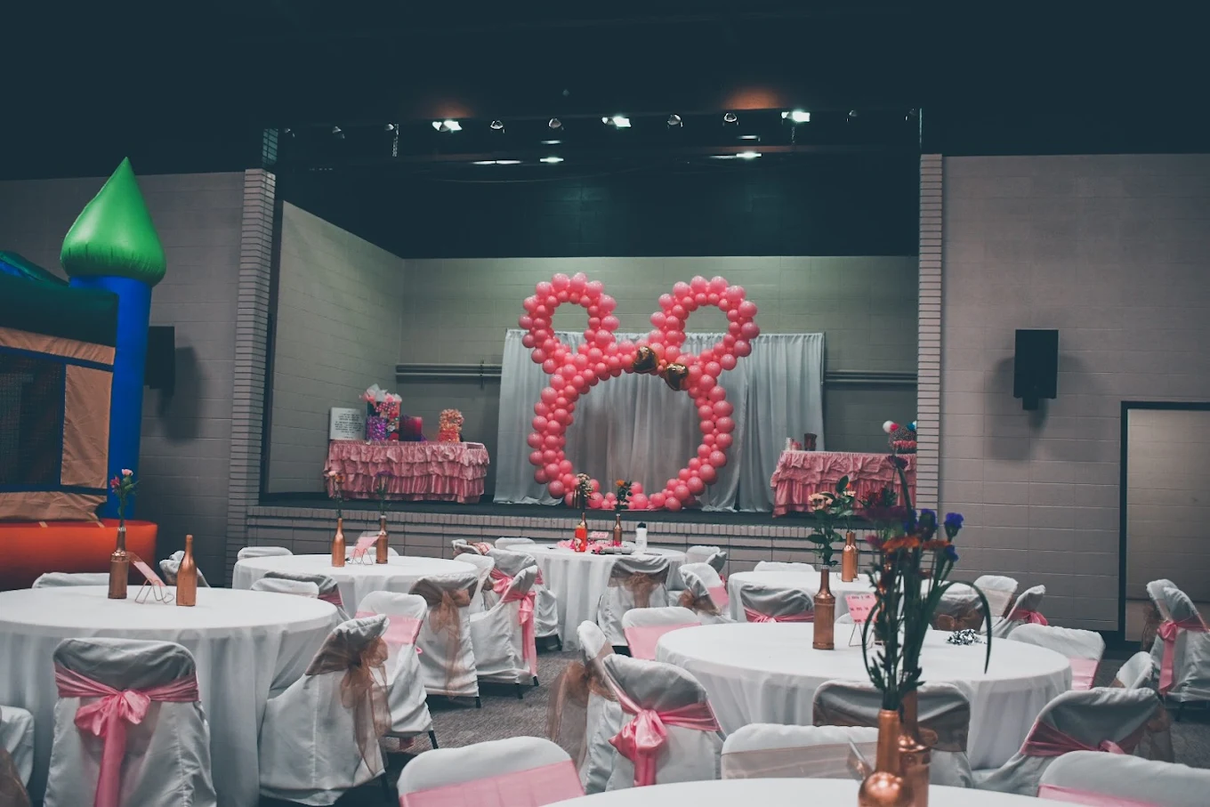 A pink balloon arch and head table set on the stage at SandHills Event Center
